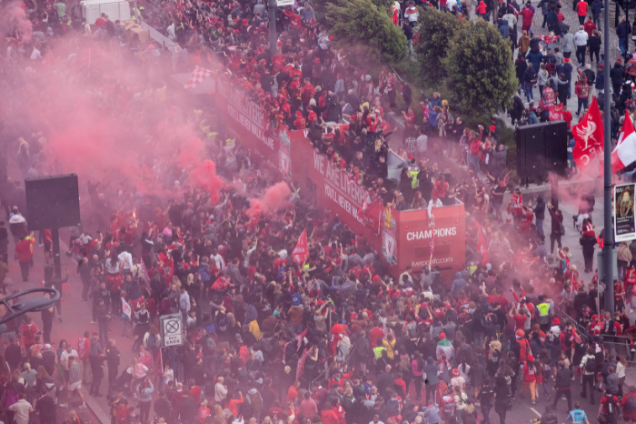 Aerial view of crowds with red open top bus in the middle with liverpool football club players on board and red smoke in the air