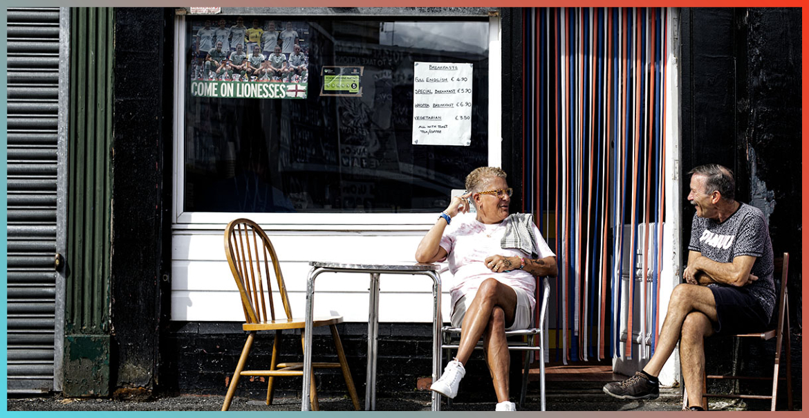 A man and a woman enjoying a conversation sitting down at a table in front of a cafe