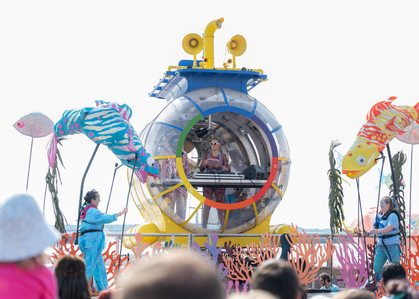 a blue an yellow submarine situated on Liverpool's Pier Head surrounded by puppet fish performing in front of a crowd