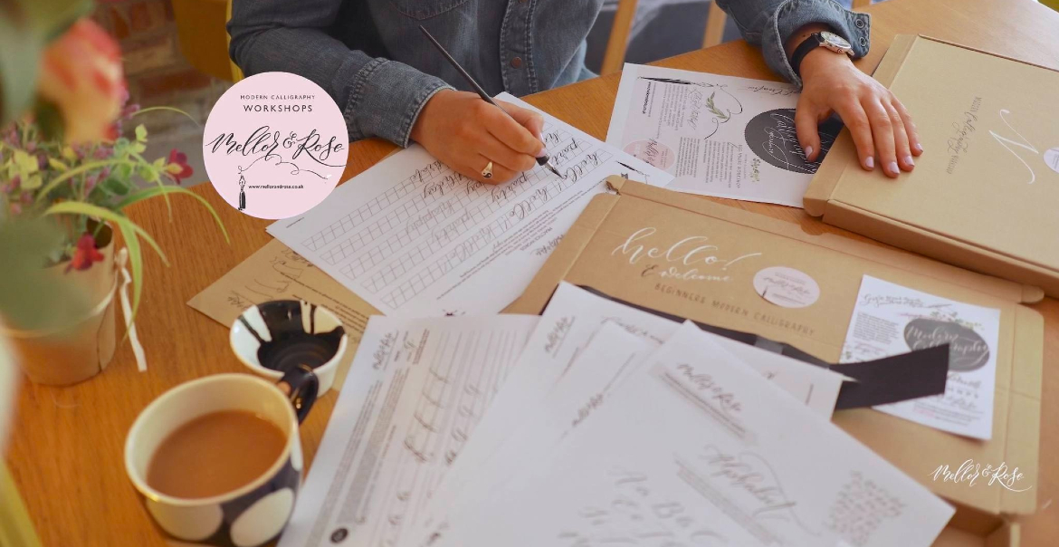 An image of people taking part in a calligraphy workshop with the focus on their hands writing on pieces of paper