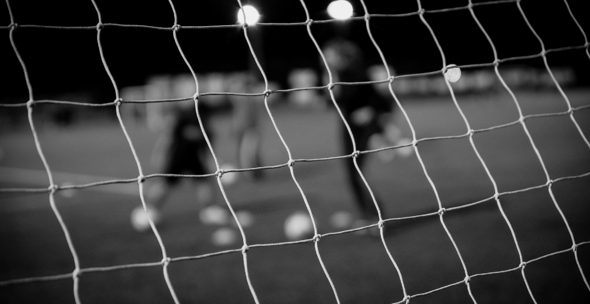 Black and white image taken behind the net of a football goal