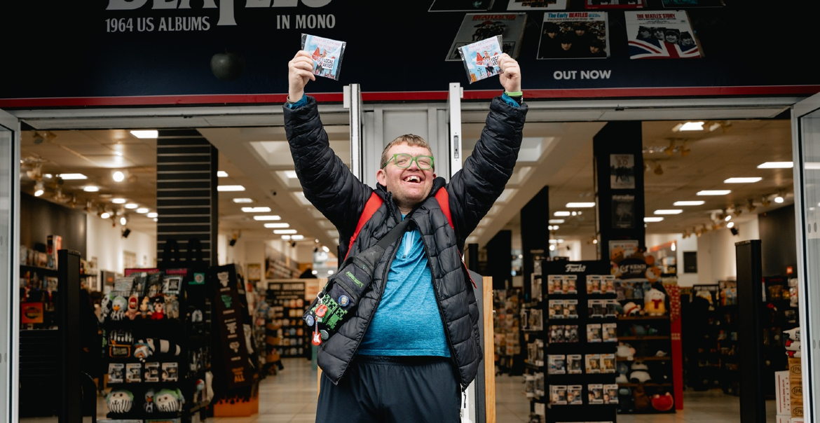 A person standing outside of a record shop holding two CDs in the air