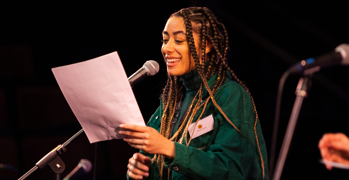 A person speaking into a microphone while reading from a piece of paper