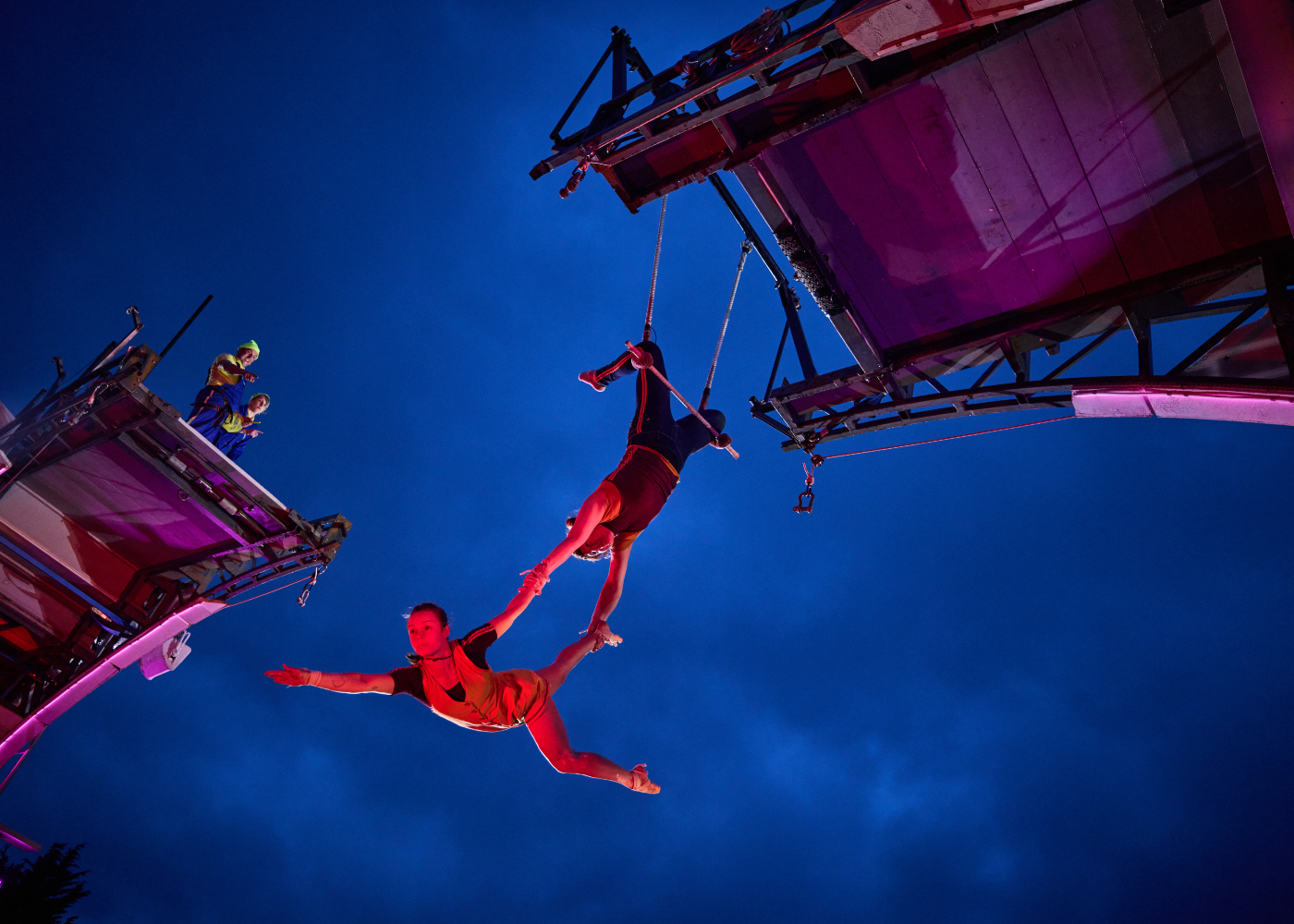 acrobatics performing mid air on a temporary bridge under the evening sky