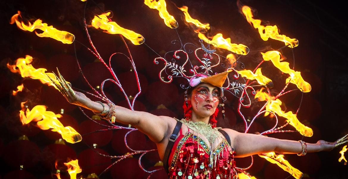 A woman performing on stage wearing a wing-like structure with fire on the ends