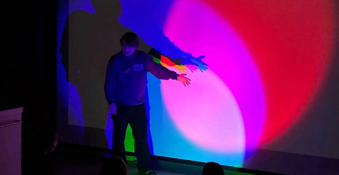 A man standing near a wall that has colourful spotlights shining onto it