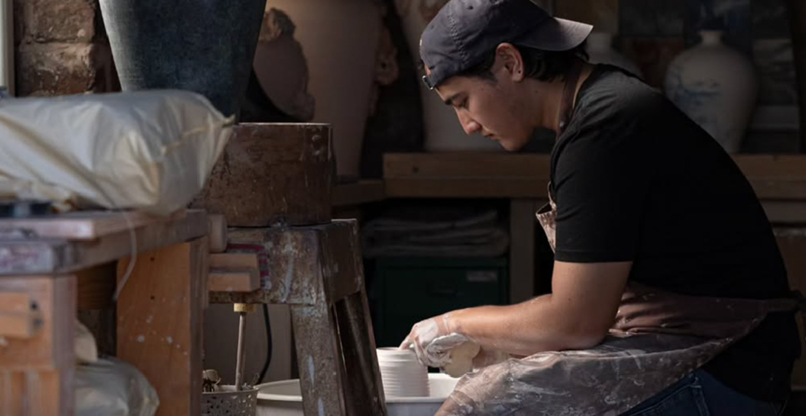 An image of a man throwing clay on a pottery wheel in an art studio