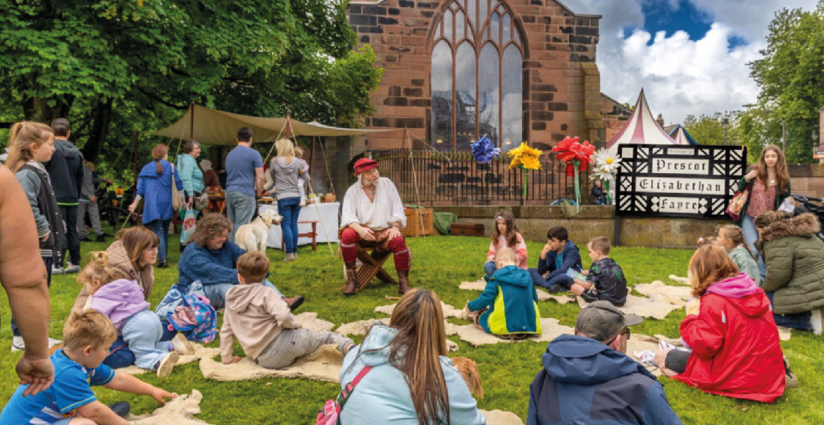 Children and adults gathered on a patch of grass at the family event - Prescot Fayre.