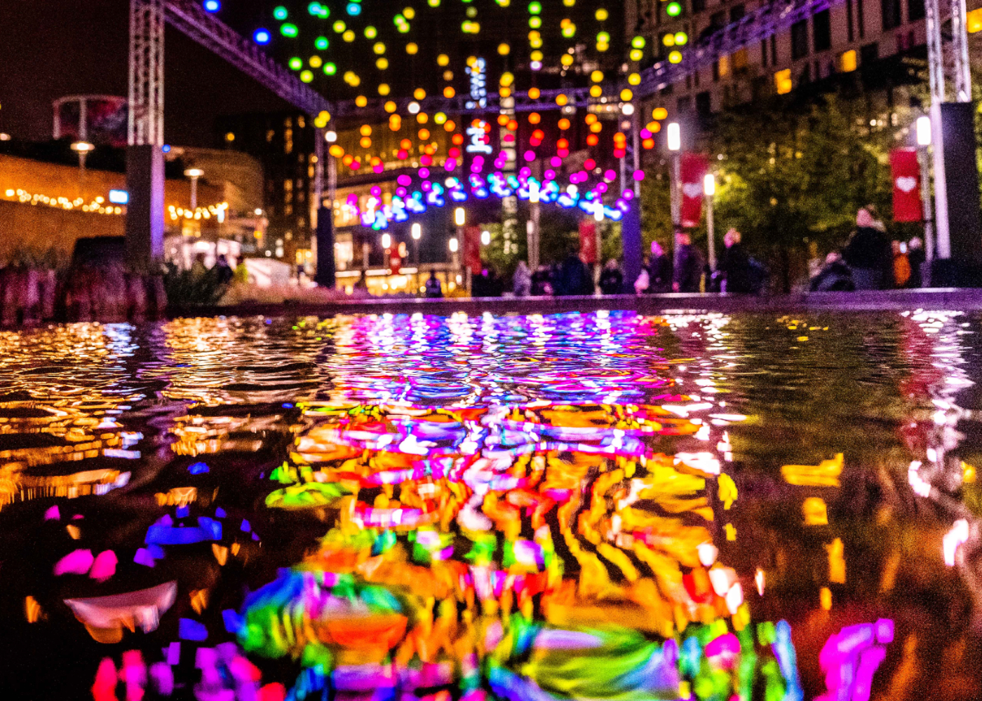 colourful light bulbs strung up high at night, reflected in a pool of water