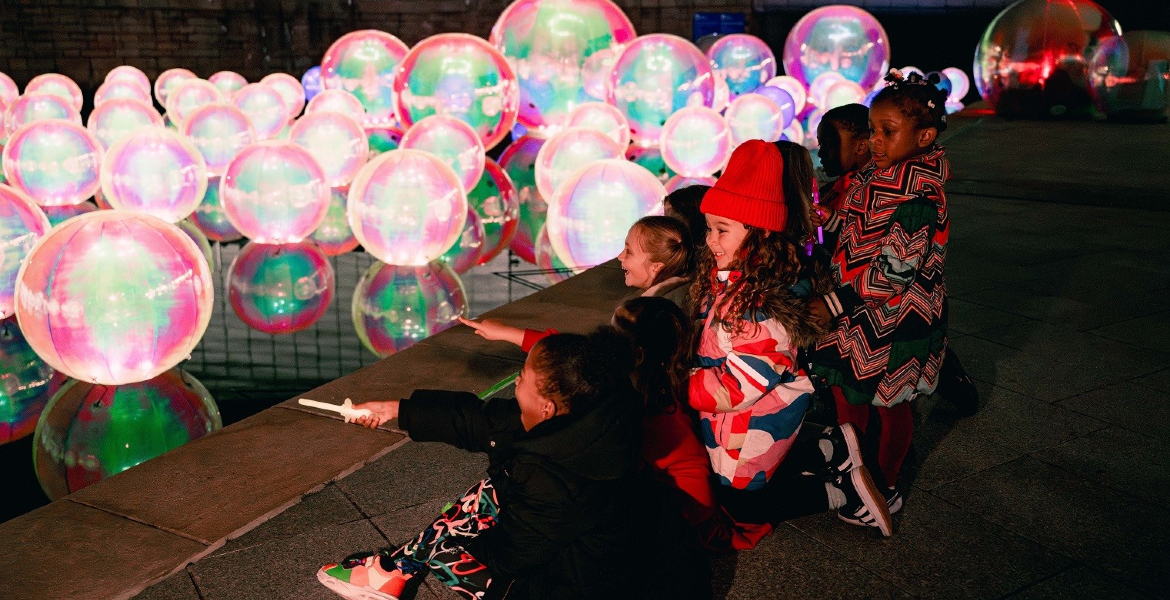 group of children looking in awe at a series of colourful orb light installations.