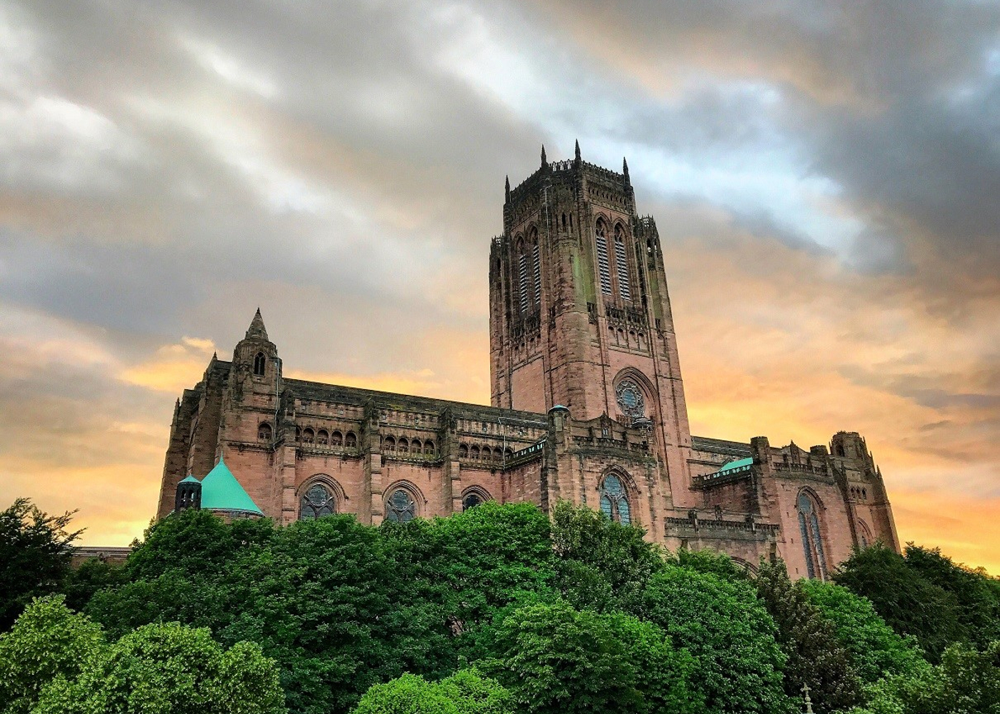 Image of Liverpool Cathedral positioned between green trees and a moody looking sky