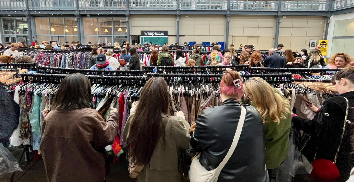 An image of customers looking at racks of vintage clothes in a large venue